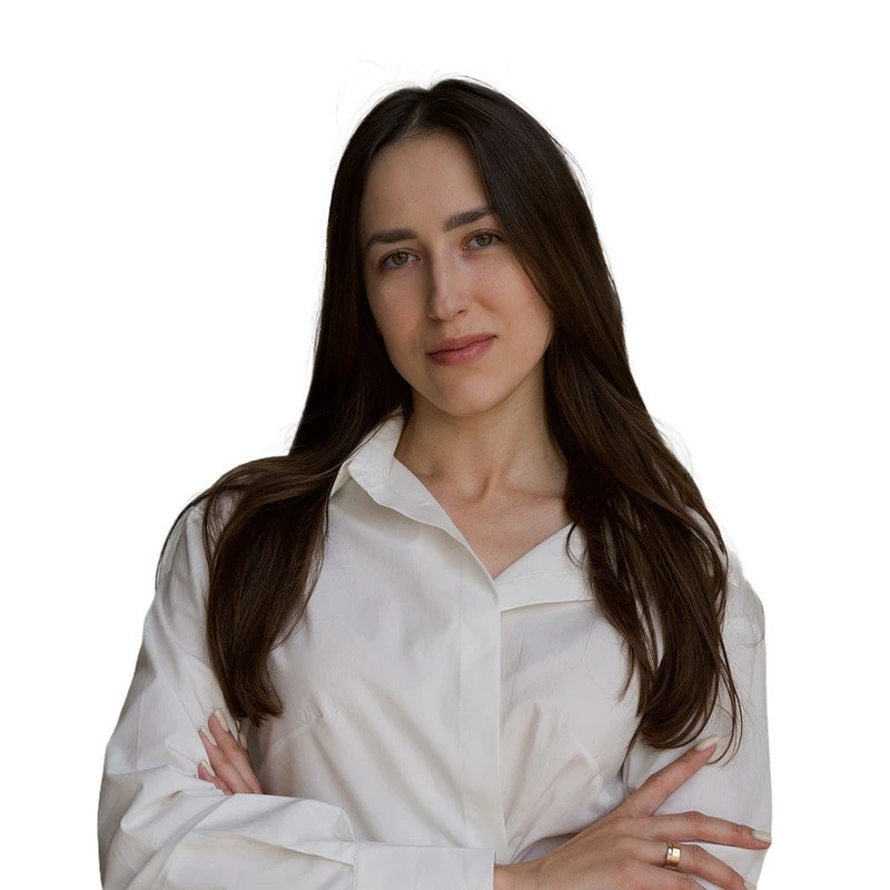 A woman with long brown hair wearing a white shirt and crossing her arms.